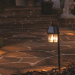 Black metal garden light shepherd with clear glass panels and warm glowing light on a shepherd hook stand