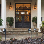 Black wrought iron front door with circular glass panel displayed near 2pk garden light shepherd hook for outdoor lighting