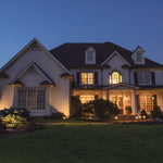 A well-lit two-story white brick house with dark shutters featuring a black metal light shepherd hook garden light