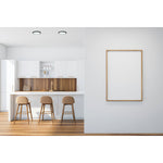 Modern kitchen with wooden bar stools and a framed poster on a white wall.