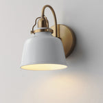A modern wall sconce light fixture with a white metal bell-shaped shade and a brushed brass/gold curved arm and circular wall mount, shown lit against a plain light gray wall.