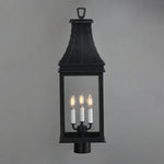 A black metal lantern-style wall light with three candle-style bulbs illuminated, shown against a plain gray background.