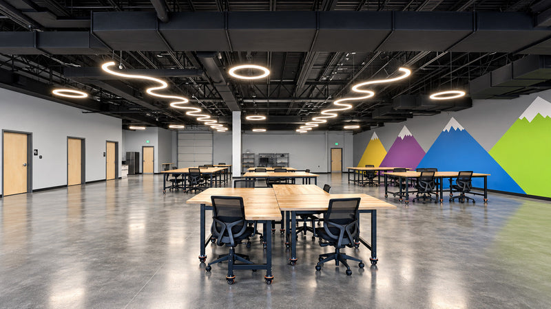 Two curved LED runs and round pendants above work tables in a children's ABA center workshop