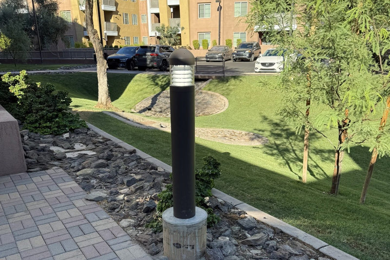 Bronze LED bollard with a dome top louver reflector beside a paver walkway at an apartment community