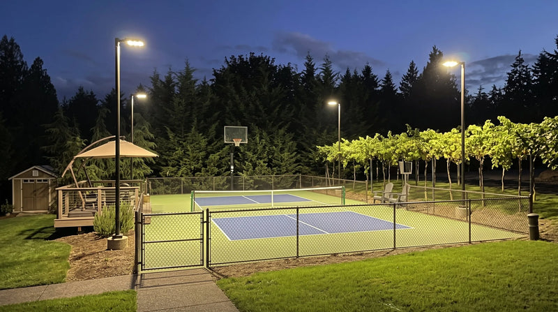 LED sports lights on four 15 ft poles lighting a fenced multi-use pickleball and basketball court at night