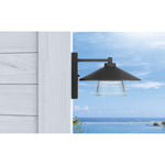 Black outdoor wall light fixture on a wooden post with a scenic background.