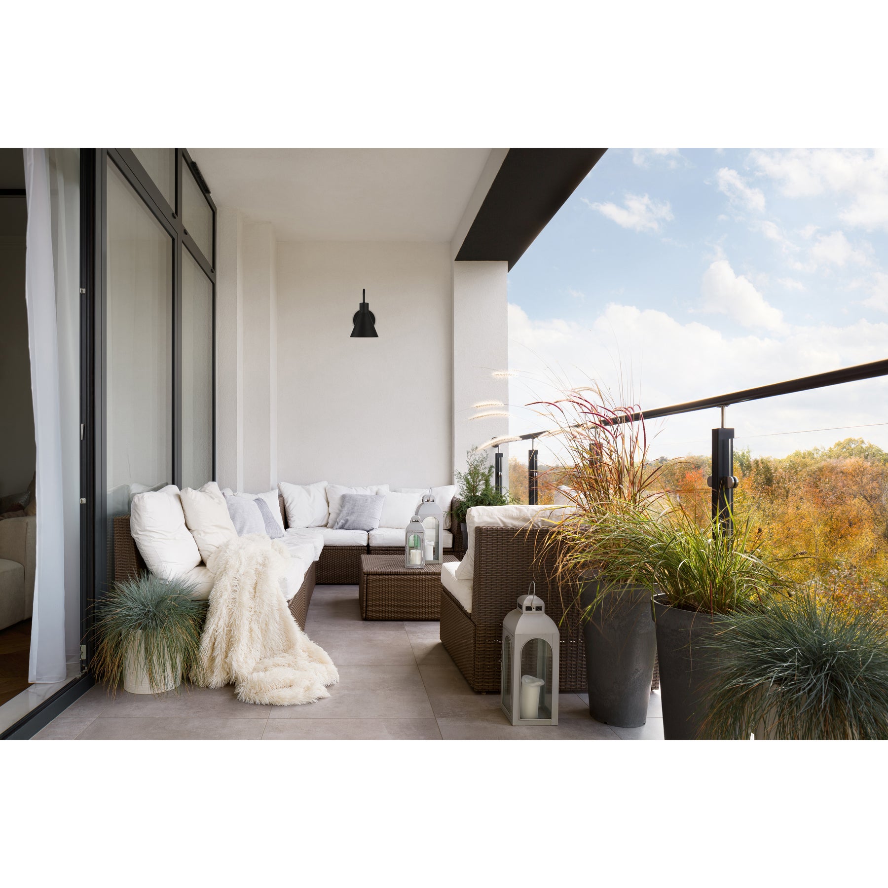 Modern outdoor living space with a sectional sofa, plants, and a view of trees and sky.