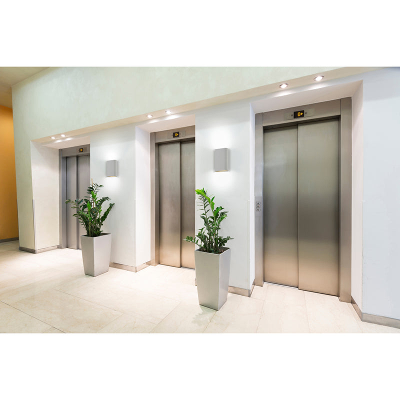 Modern elevator lobby with three elevators, potted plants, and an LED Wall Sconce lighting.