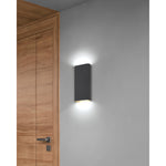 Black wall-mounted light fixture on a gray wall next to a wooden door.
