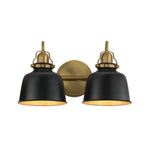 A two-light wall sconce with matte black bell-shaped shades and antique brass hardware, including a round backplate and decorative caps, shown against a plain white background.