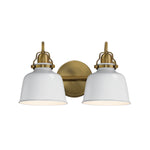 A two-light wall sconce with white bell-shaped glass shades and an antique brass backplate and hardware, shown against a plain white background.