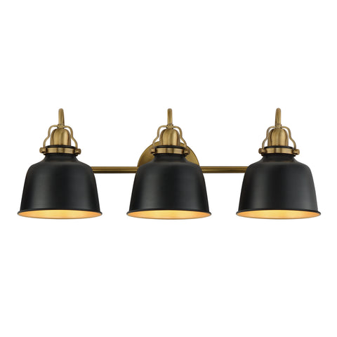 A three-light vanity wall sconce with matte black bell-shaped shades and an antique brass horizontal bar and mounting hardware, shown against a plain white background.