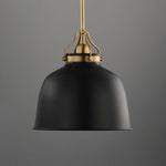 A modern pendant light with a matte black dome-shaped shade and an antique brass suspension hardware piece, shown against a solid gray background.