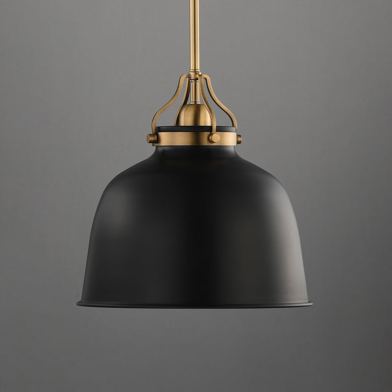 A modern pendant light with a matte black dome-shaped shade and an antique brass suspension hardware piece, shown against a solid gray background.