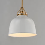 A modern pendant light with a large white dome-shaped shade, a warm white glowing interior, and antique brass hardware at the top, suspended against a solid gray background.