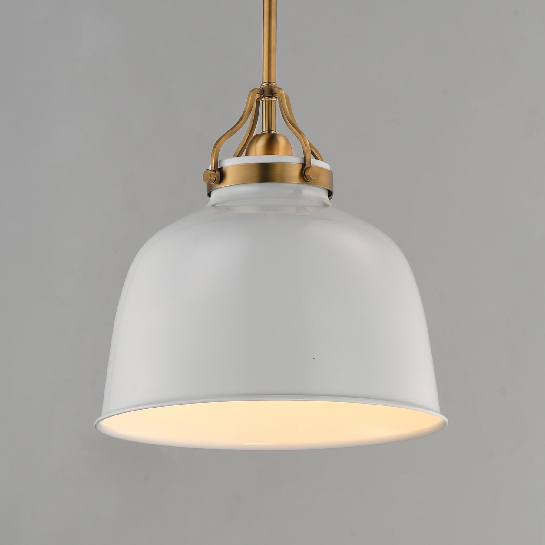 A modern pendant light with a large white dome-shaped shade, a warm white glowing interior, and antique brass hardware at the top, suspended against a solid gray background.