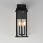 Black outdoor wall light fixture with three illuminated bulbs on a gray background