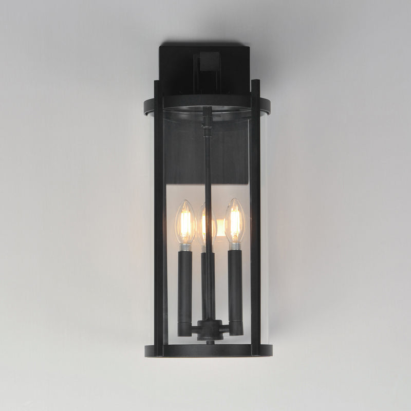 Black outdoor wall light fixture with three illuminated bulbs on a gray background