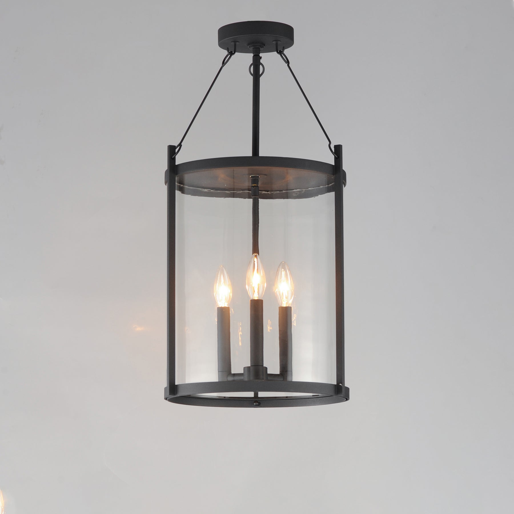 Black pendant light fixture with three lit bulbs on a gray background