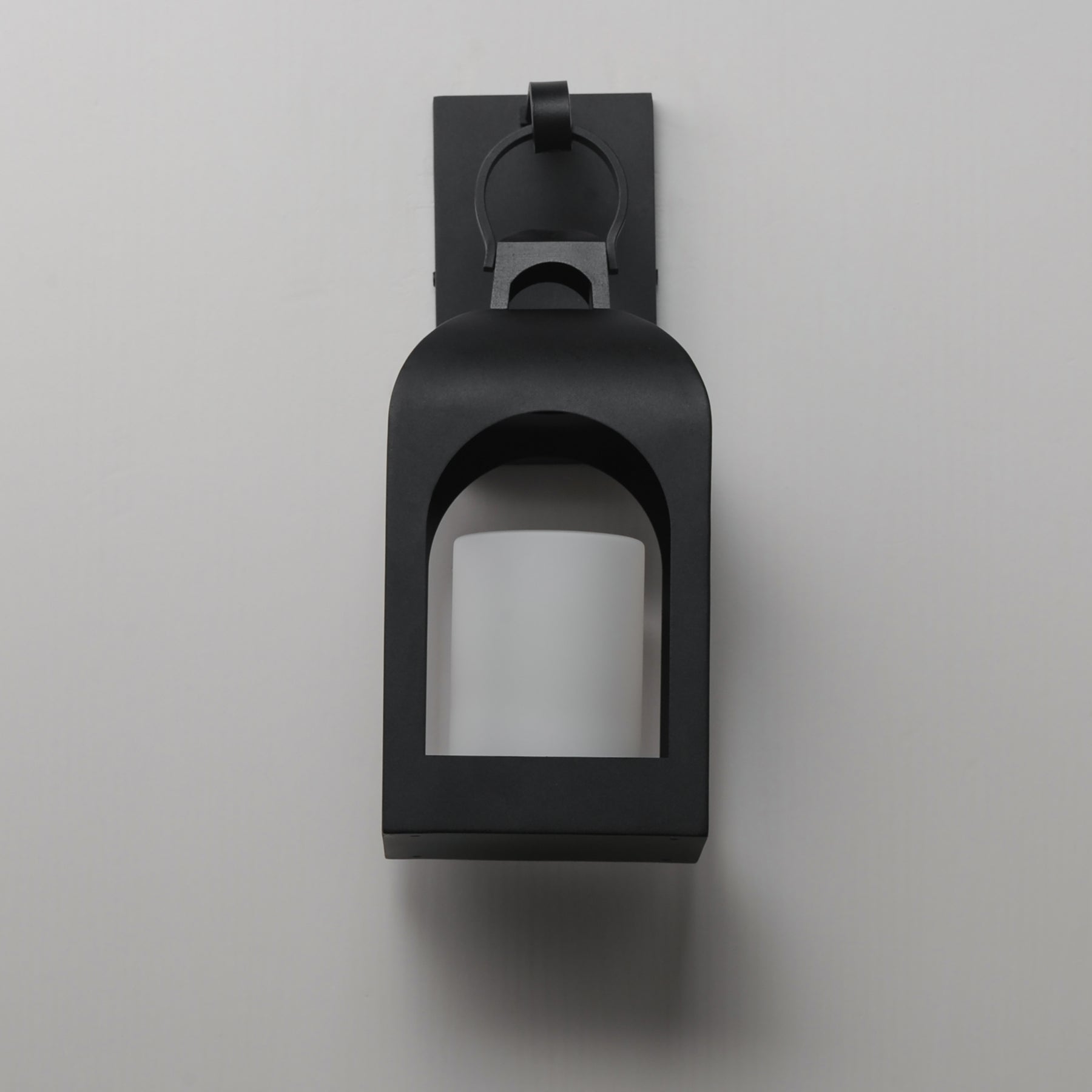 A matte black outdoor wall sconce with a square frame and arched opening, mounted on a light gray wall.