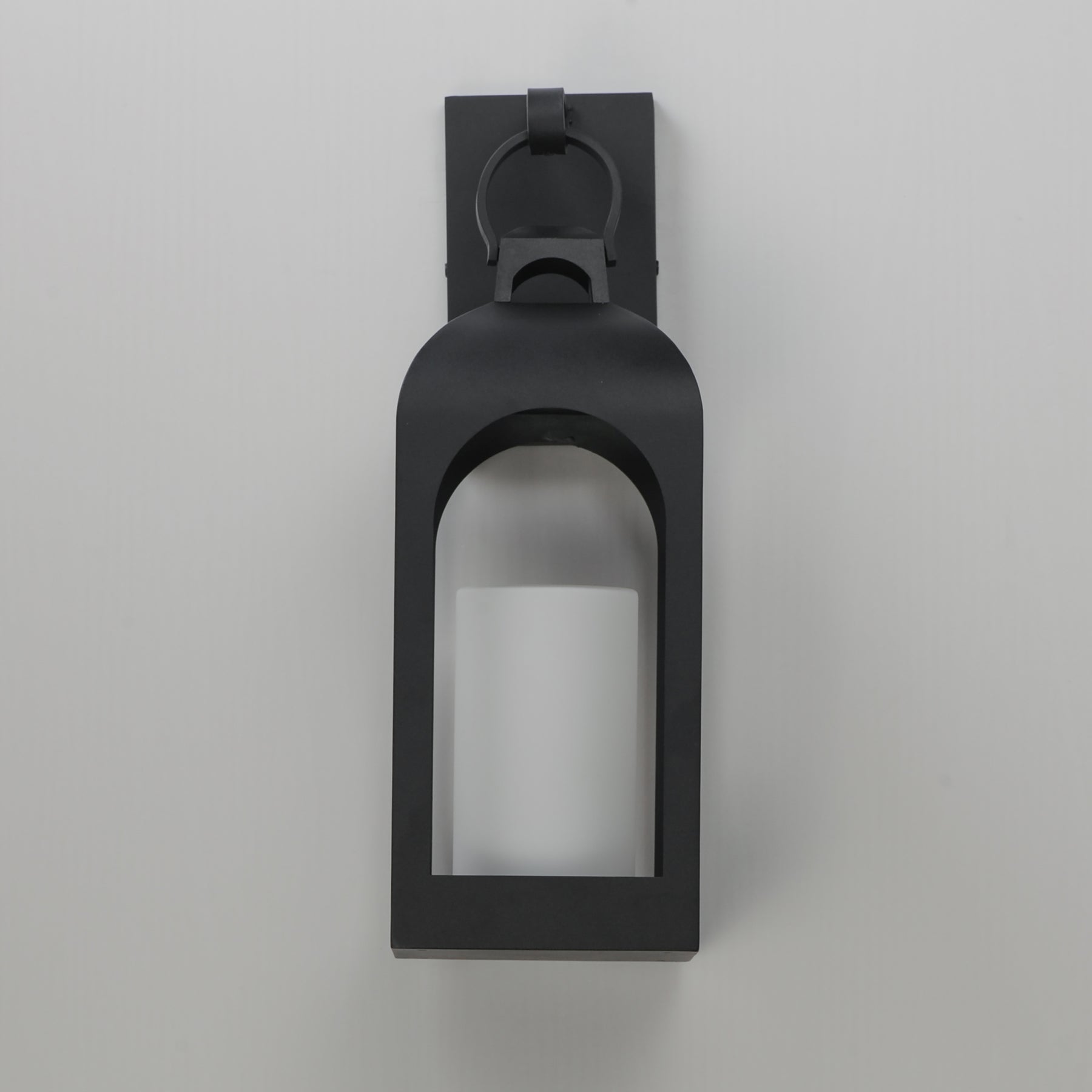 A matte black outdoor wall sconce with a lantern-style frame and a glass panel, shown against a neutral light gray background.