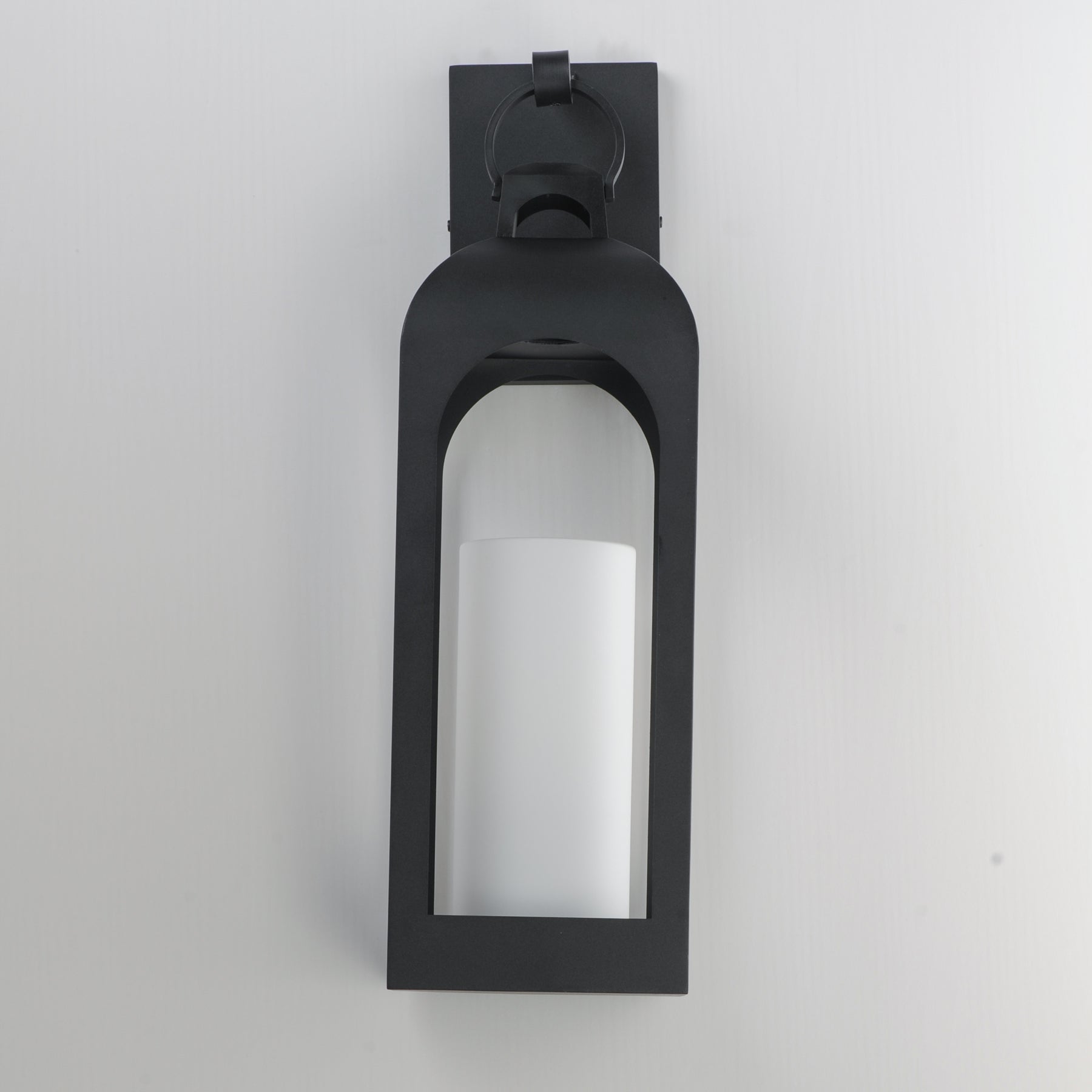 A modern black outdoor wall sconce with a frosted white cylindrical glass shade, mounted on a plain light gray wall.