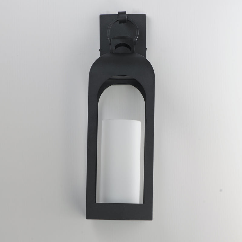 A modern black outdoor wall sconce with a frosted white cylindrical glass shade, mounted on a plain light gray wall.