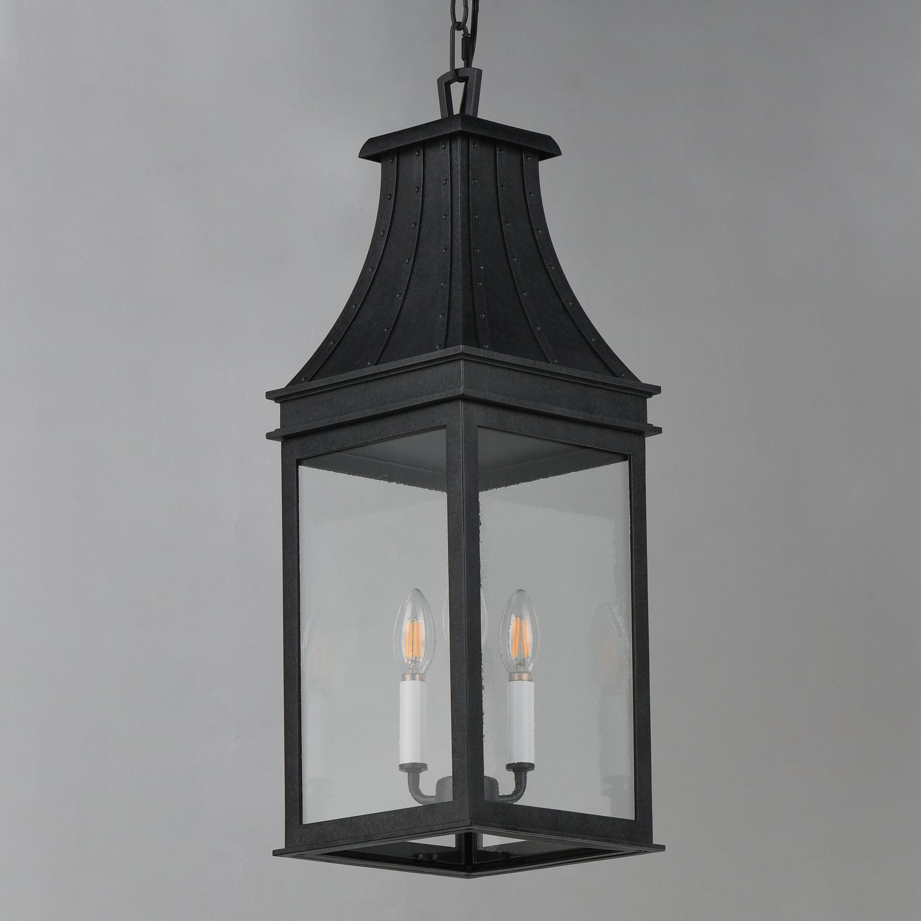 A black metal lantern-style pendant light with clear glass panels and two visible candle-style bulbs, hanging against a plain light gray background.