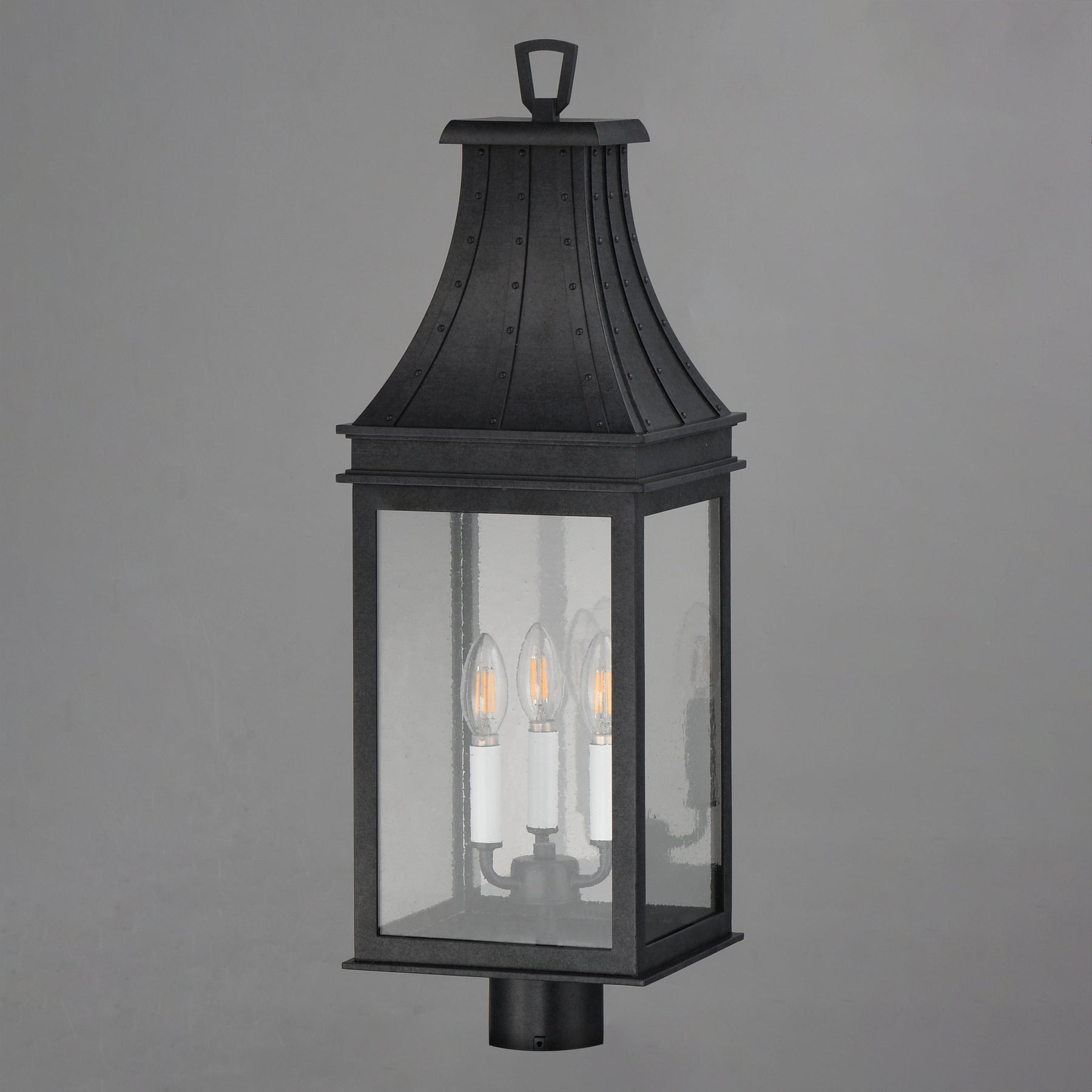 A black outdoor lantern-style wall light with three visible candle-style bulbs inside a rectangular glass enclosure, shown against a plain gray background.
