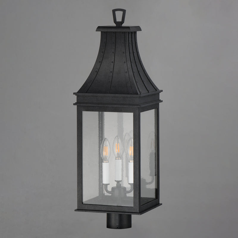 A black outdoor lantern-style wall light with three visible candle-style bulbs inside a rectangular glass enclosure, shown against a plain gray background.