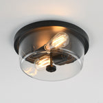 A modern semi-flush mount ceiling light fixture with a round black metal base, a clear glass dome shade, and two visible warm Edison-style bulbs.