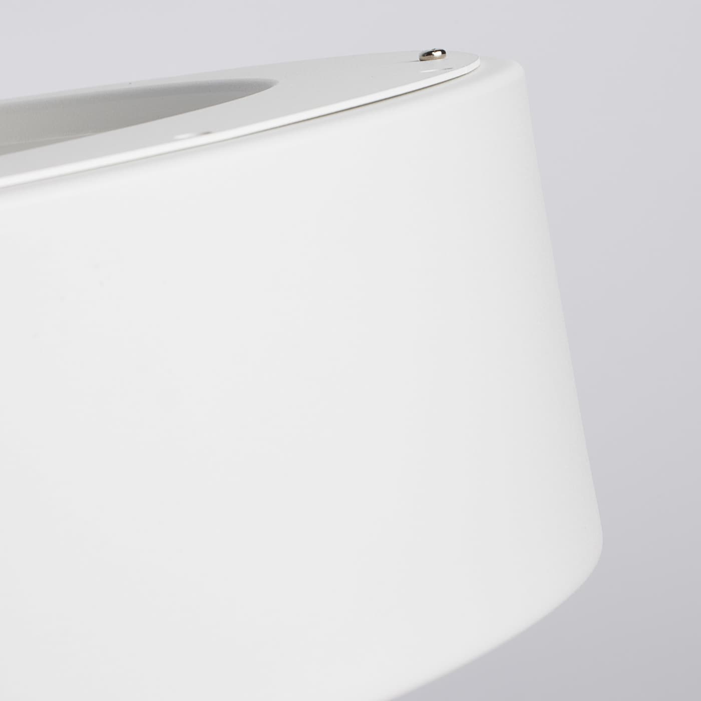 Close-up of a white cylindrical lampshade or container with a smooth matte finish, showing a small metal screw detail at the top against a light gray background.