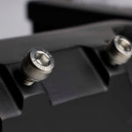 Close-up of a black textured mounting surface with two silver metal hex screws, one in sharp focus and the other blurred in the background.