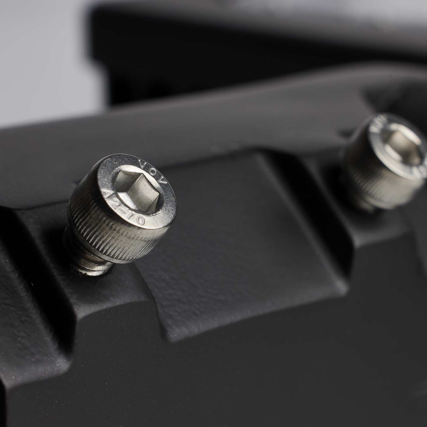 Close-up of a black textured mounting surface with two silver metal hex screws, one in sharp focus and the other blurred in the background.