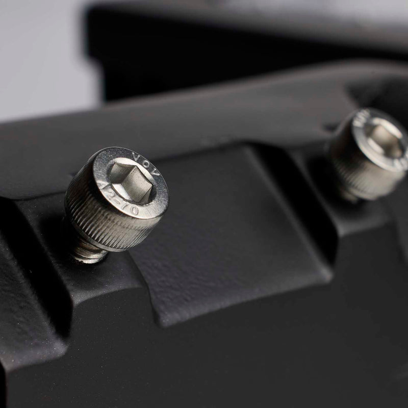 Close-up of a black textured mounting surface with two silver metal hex screws, one in sharp focus and the other blurred in the background.