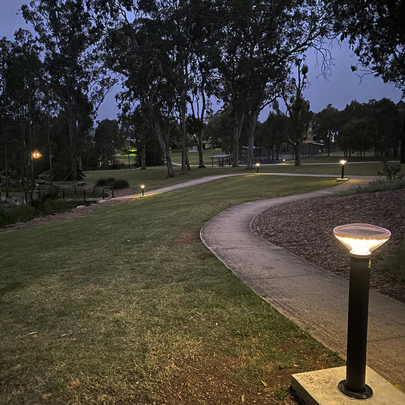 A modern black solar vandal resistant bollard light with a pink dome top emitting warm 588 lumens illumination