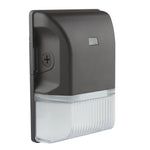 A wall-mounted outdoor light fixture with a matte black top housing a small rectangular sensor or label, and a ribbed clear lower housing, shown on a plain white background.