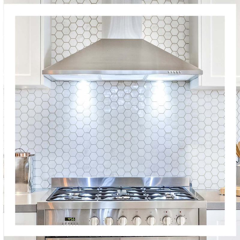 A stainless steel gas range and matching range hood installed in a kitchen with white hexagonal mosaic tile backsplash and white cabinetry.