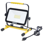 A SATCO portable LED work light with a yellow and black metal stand, featuring a yellow carrying handle and a black power cord with a US plug, shown on a white background.