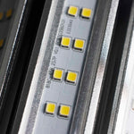 Close-up of an LED light strip showing multiple small yellow LED chips on a silver metal base with printed technical specifications.