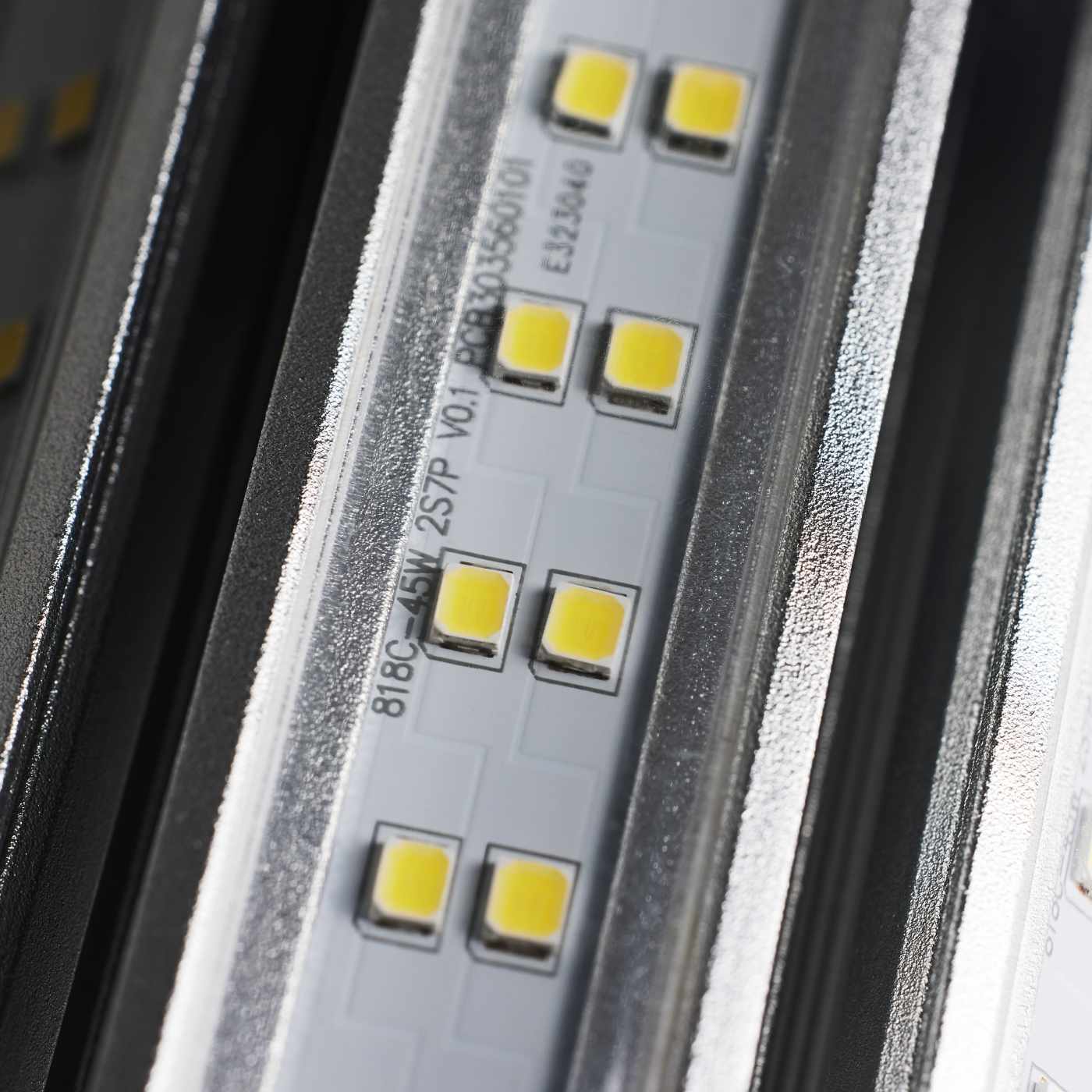 Close-up of an LED light strip showing multiple small yellow LED chips on a silver metal base with printed technical specifications.