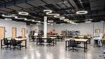 A large, modern open-plan office space with awesome curved led lighting, multiple light wood desks, black office chairs, and a high ceiling with exposed industrial ductwork and multiple circular pendant lights.