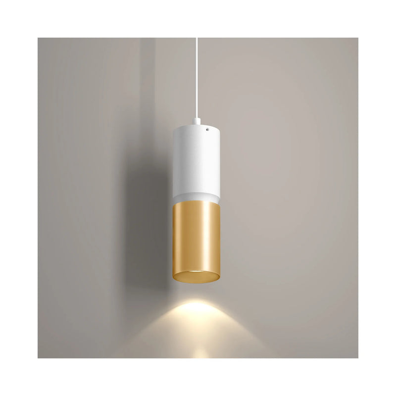 A modern pendant light with a white upper cylinder and a brushed gold lower cylinder, shown illuminated against a neutral gray wall.