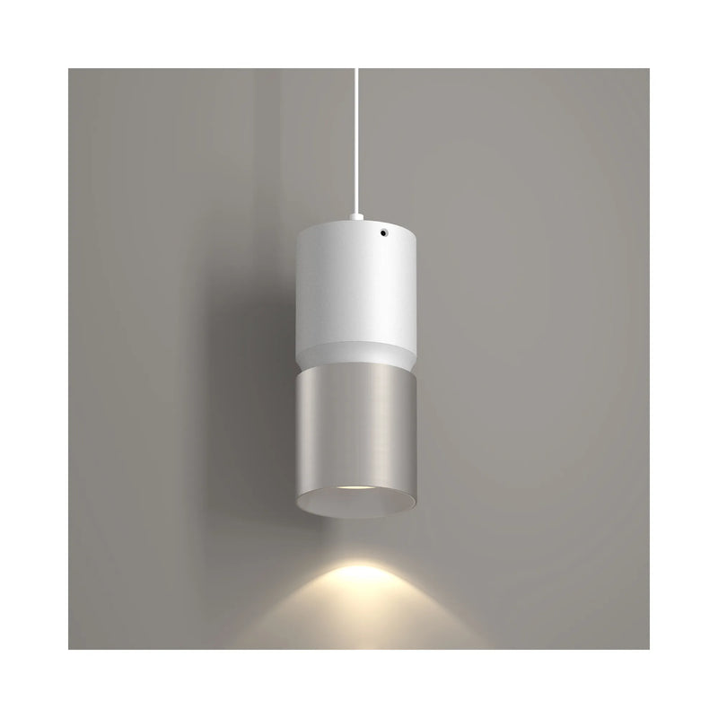 A modern cylindrical pendant light fixture with a white upper section and a brushed nickel lower section, shown hanging against a neutral gray wall with a warm light beam directed downward.