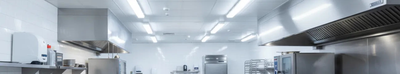 Bright commercial kitchen with stainless steel equipment and vapor proof ceiling lights.